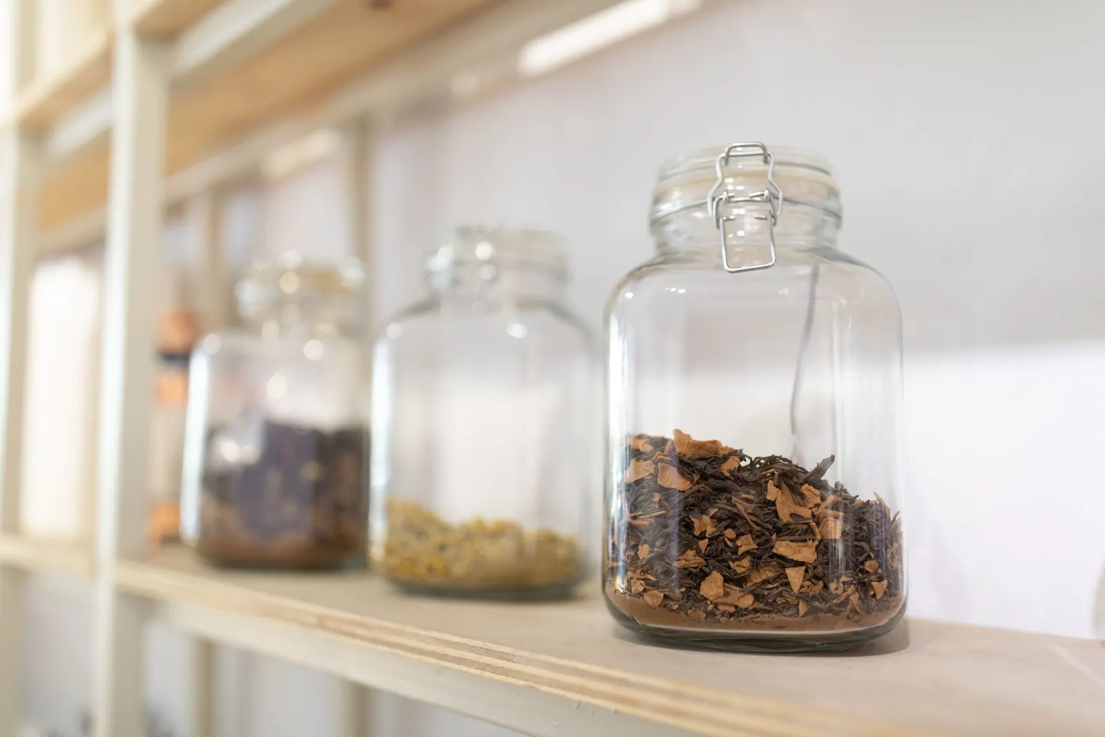 Glass jars of dried botanicals resting on a plain shelf