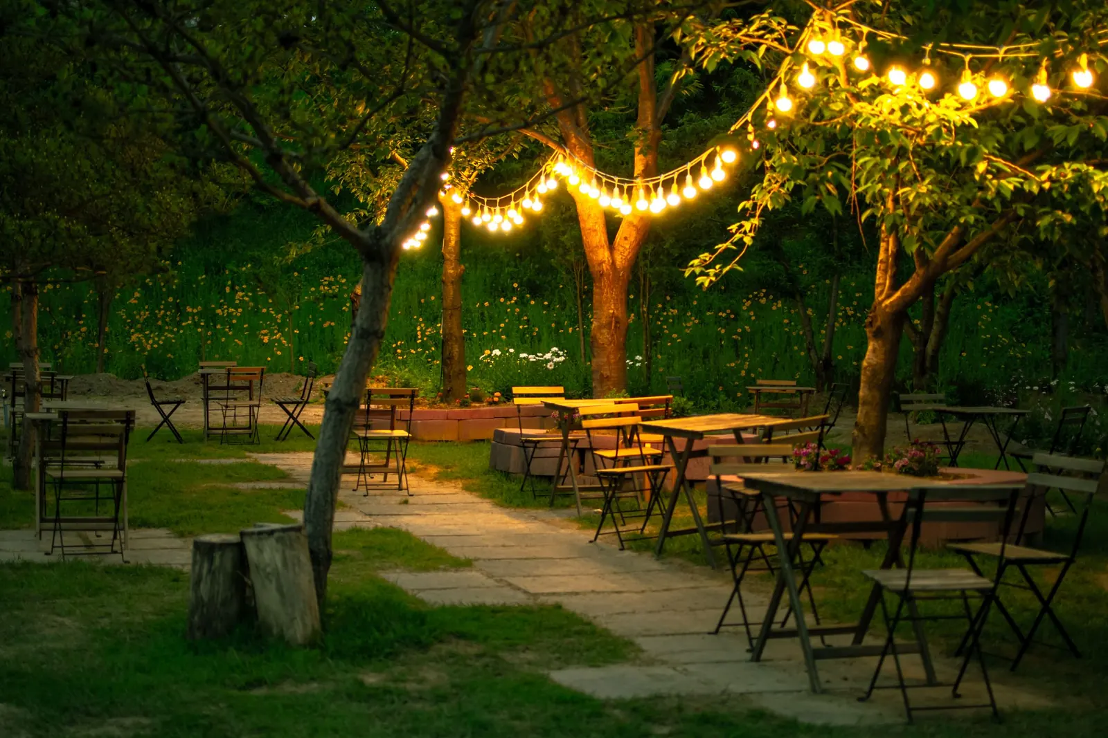 A garden terrace set for dinner under string lights